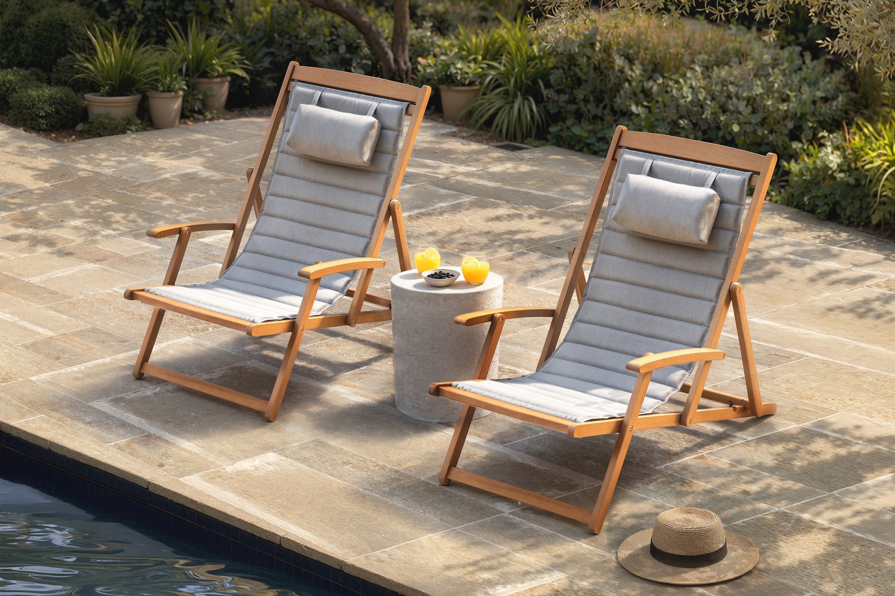 Two wooden sling chairs with gray fabric on a stone patio by a pool.