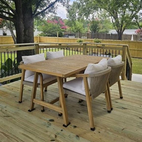 Wooden outdoor dining set with chairs on a deck surrounded by trees and greenery.